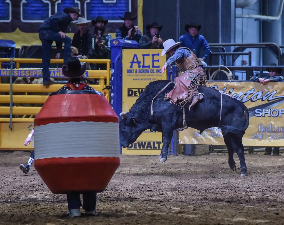 Mississippian Lucas Mooningham of Goldwater and his bull Tomahawk compete in the Bull Riding event at the Dixie National Rodeo as Dusty the Rodeo Clown looks on at the State Fairgrounds in Jackson, Miss., Sunday, February 12, 2023.