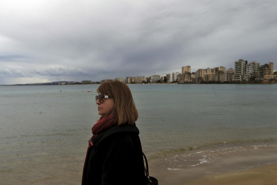FILE - In this Sunday, Jan 6, 2019 file photo, a Greek Cypriot woman stands at the beach before the epiphany ceremony to bless the sea waters at Famagousta or Varosia beach in the abandoned city, seen in the background, in Cyprus. The man who hopes to be the next leader of the breakaway Turkish state in northern Cyprus, Ersin Tatar says ongoing tensions over drilling for oil and gas would fade if Greek Cypriots drop their objections and agree to divvy up the country’s territorial waters and drilling rights. (AP Photo/Petros Karadjias, File)