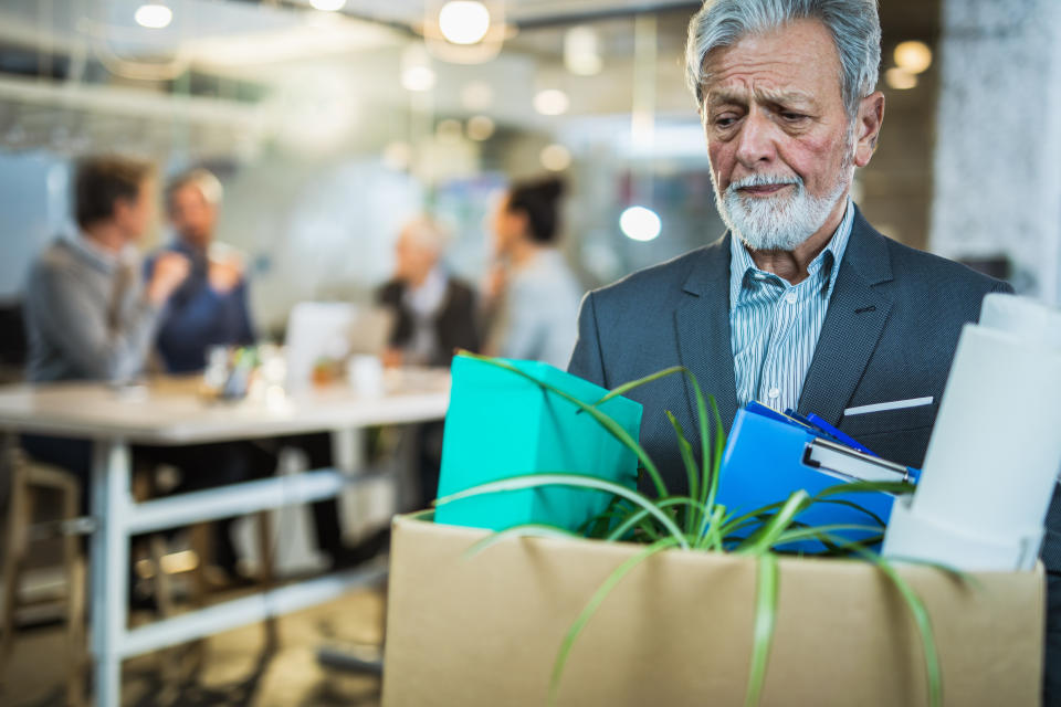 Sad mature businessman going to retirement and leaving the office while carrying his belongings.