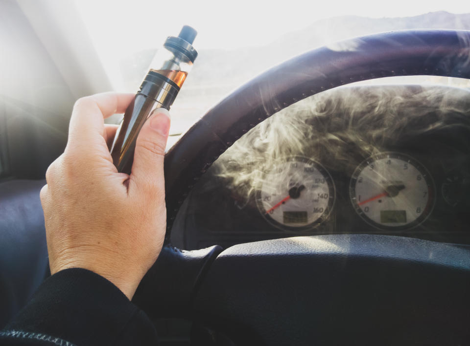 A stock image of a woman holding an e-cigarette by the steering wheel. A patient has become the first person in the US to die from vaping, according to Centers for Disease Control and Prevention.