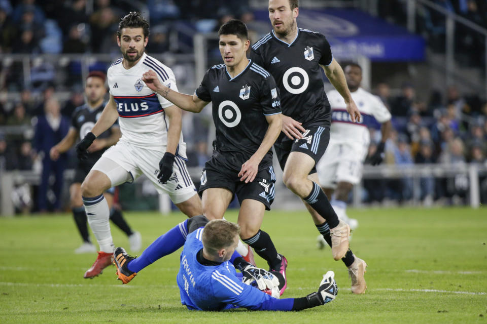 Minnesota United goalkeeper Clint Irwin (1) makes a sliding save as United defenders Miguel Tapias (4) and Brent Kallman (14) make sure Vancouver Whitecaps forward Brian White (24) doesn't get to the ball in the first half of an MLS soccer game Saturday, March 25, 2023, in St. Paul, Minn. (AP Photo/Andy Clayton-King)