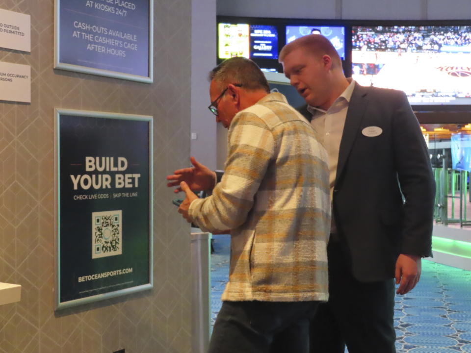 FILE - An employee at the Ocean Casino Resort in Atlantic City N.J. helps a customer use a cell phone to scan a sports betting code on Feb. 6, 2023. Americans have bet over $220 billion on sports with legal gambling outlets in the five years since the U.S. Supreme Court cleared the way for all 50 states to offer it. (AP Photo/Wayne Parry)