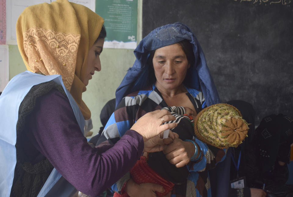 In this Saturday, Oct. 20, 2018, photo, an employee of Independent Elections Commission, left, sticks a biometric sticker on a mother, who is feeding her baby, before casting her vote at a polling station in Faizabad, center of northern Badakhshan province, Afghanistan. Badakhshan province, Afghanistan’s parliamentary elections entered a second day on Sunday, Oct. 21, 2018, following violence and chaos that caused delays and interruptions on the first day of polling. (AP Photo/Omer Abrar)