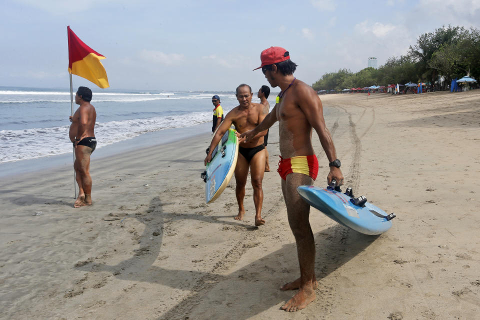 Lifeguards carry their surfboards during a beach rescue drill on Kuta Beach, Bali, Indonesia on Thursday, Oct. 28, 2021. Indonesians are looking ahead warily toward the upcoming holiday travel season, anxious for critical tourist spending but at the same time worried that an influx of millions of visitors could lead to a new coronavirus wave just as the pandemic seems to be getting better. (AP Photo/Firdia Lisnawati)