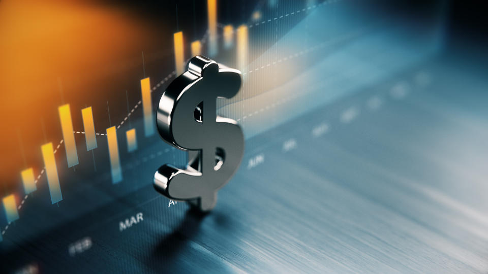 American dollar symbol standing on wood surface in front of a graph. (PHOTO: Getty Creative)