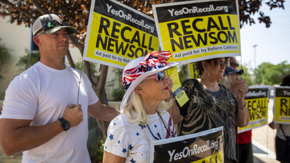 Protesters wearing sunglasses but not face masks hold signs reading: Yesonrecall.org, Recall Newsom, Ad paid for by Reform California