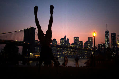 Yukihiro Yoshida from Nagoya, Japan, tries to imitate a skyscraper in front of the Brooklyn Bridge and the Lower Manhattan skyline from Brooklyn borough of New York September 10, 2013. REUTERS/Adrees Latif/Files