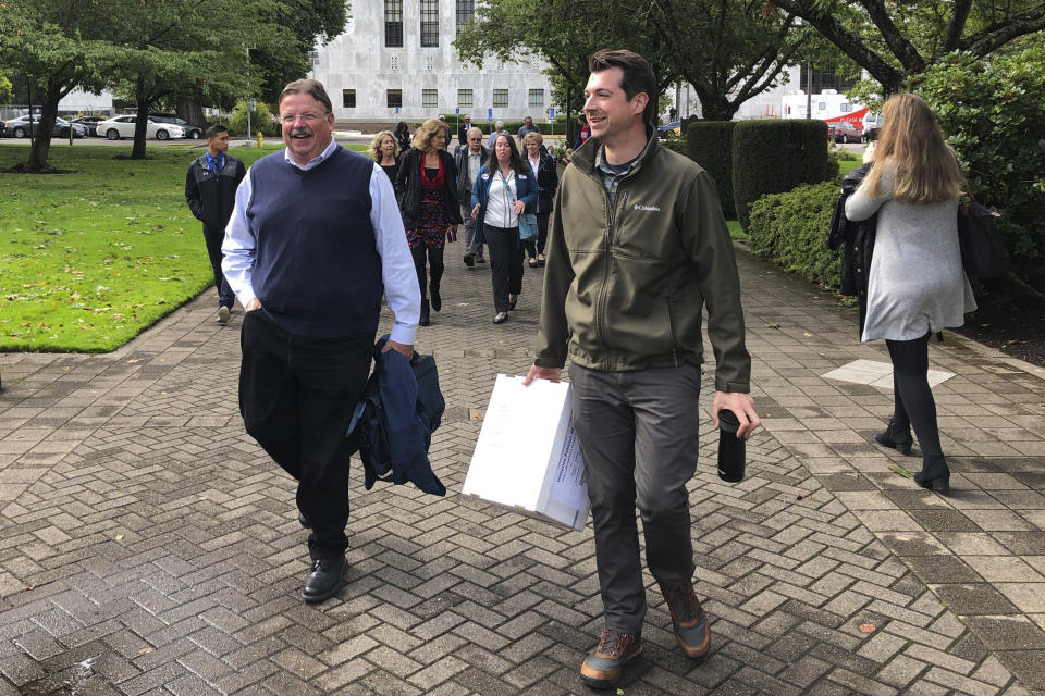 Joe Emmons, right, a signature gatherer for a proposed ballot measure requiring the safe storage of weapons, and Otto Schell, legislative director of the Oregon PTA, walk with other supporters on Wednesday, Sept. 18, 2019, to the state elections office in Salem, Ore., to deliver 2,000 signatures backing the proposed ballot measure. Emmons is carrying a box containing the signatures. (AP Photo/Andrew Selsky)