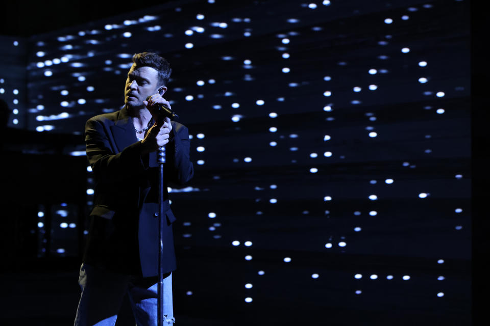 Justin Timberlake holds onto a microphone stand as he sings.