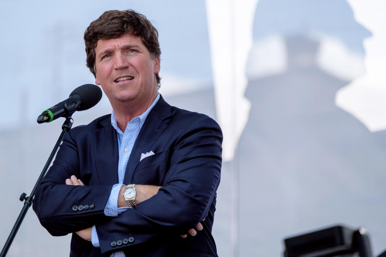 Tucker Carlson stands at a microphone.