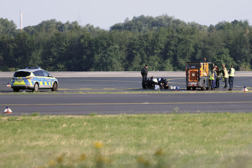 Police officers and security personnel stand on the airfield and try to detach activists of the group Last Generation who have stuck themselves to the asphalt in the airport area, in Duesseldorf, Germany, Thursday July 13, 2023. (David Young/dpa via AP)