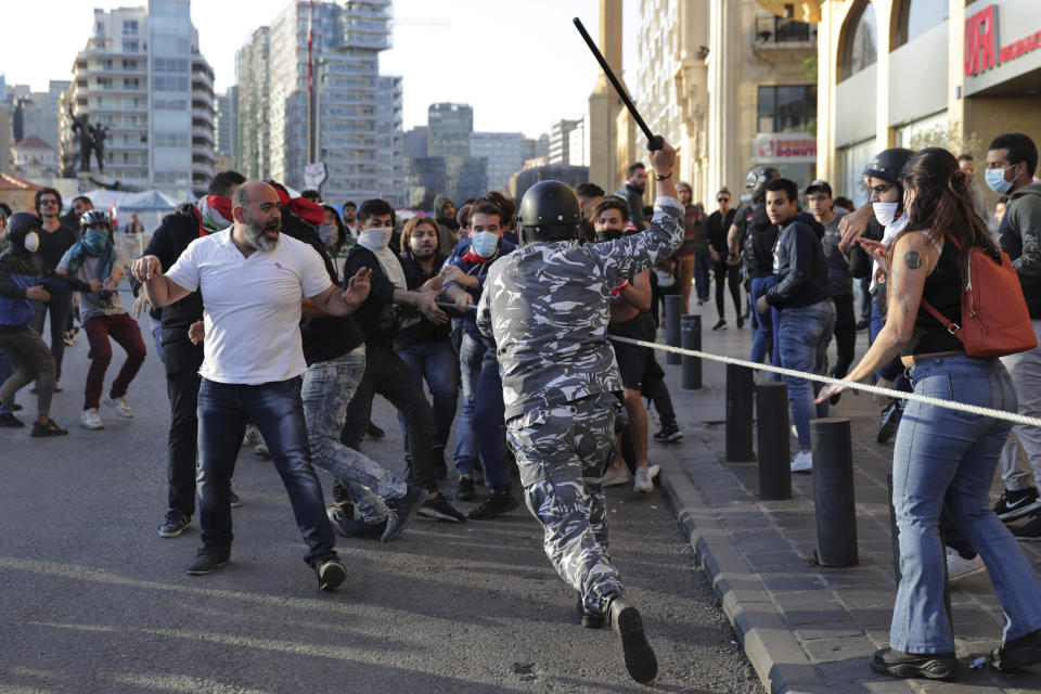 A police officer raises his baton to anti-government protesters during clashes during a protest in downtown Beirut, Lebanon, Tuesday, Nov. 19, 2019. Scuffles have broken out in central Beirut as hundreds of anti-government protesters tried to prevent lawmakers from reaching Parliament. (AP Photo/Hassan Ammar)