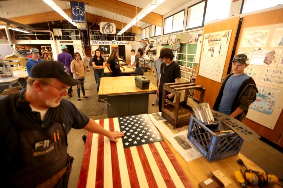 A woodworking teacher looks over students' creation of a U.S. flag.