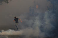 An anti-government protester runs amid tear gas fired by riot police during a protest marking the first anniversary of the massive blast at Beirut's port, near Parliament Square, In Beirut, Lebanon, Wednesday, Aug. 4, 2021. United in grief and anger, families of the victims and other Lebanese came out into the streets of Beirut on Wednesday to demand accountability as banks, businesses and government offices shuttered to mark one year since the horrific explosion. (AP Photo/Bilal Hussein)