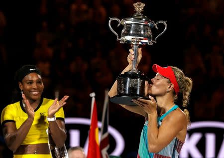 Germany's Angelique Kerber kisses the trophy as Serena Williams of the U.S. claps after Kerber won their final match at the Australian Open tennis tournament at Melbourne Park, Australia, January 30, 2016. REUTERS/Tyrone Siu