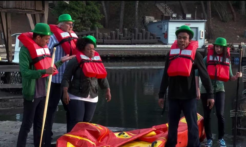 The study group, except Jeff and Britta, standing by a deflated raft in life vests, in "Community"