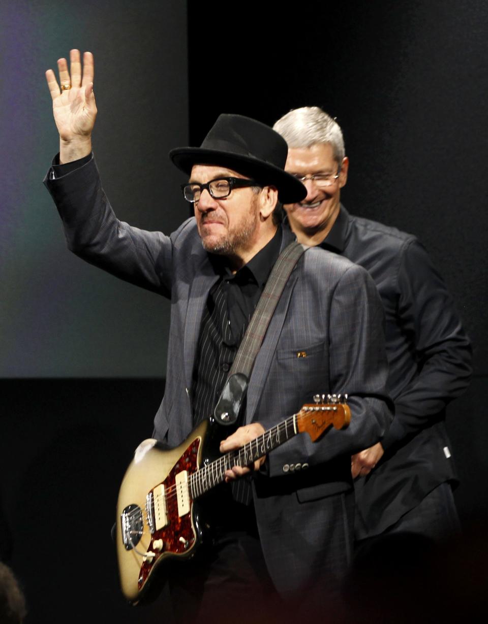 Singer Elvis Costello (L) waves from the stage with Apple Inc CEO Tim Cook (R) during Apple Inc's media event in Cupertino, California September 10, 2013. REUTERS/Stephen Lam (UNITED STATES - Tags: BUSINESS SCIENCE TECHNOLOGY BUSINESS TELECOMS ENTERTAINMENT)