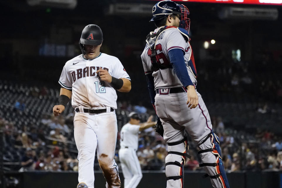 Arizona Diamondbacks' Daulton Varsho (12) scores on a ground out hit by Pavin Smith during the third inning of a baseball game as catcher Travis d'Arnaud looks on, Tuesday, Sept. 21, 2021, in Phoenix. (AP Photo/Matt York)