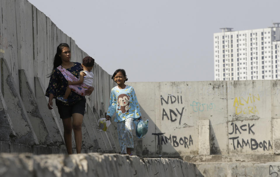 People walk near of a giant sea wall which is used as a barrier to prevent sea water from flowing into land and cause flooding in Jakarta, Indonesia, Saturday, July 27, 2019. Indonesia's President Joko Widodo said in an interview that he wants to see the speedy construction of the giant sea wall to save the low-lying capital of Jakarta from sinking under the sea, giving renewed backing to a long-delayed multi-billion-dollar mega project. (AP Photo/Achmad Ibrahim)