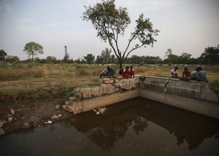 Residents sit atop a crumbling wall beside a pond near the abandoned former Union Carbide pesticide plant in Bhopal November 11, 2014. REUTERS/Danish Siddiqui