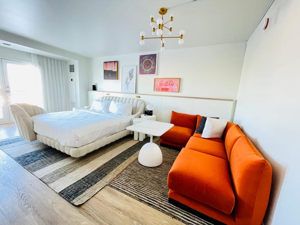 white, airy hotel room with bright orange couch and funky gold chandelier