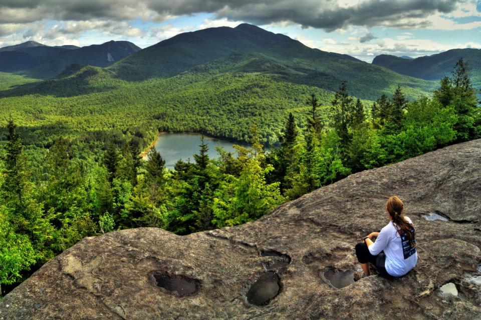 A hiker sits to take in the view of the Adirondack High Peaks