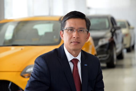 Thai-Tang is shown standing in front of several Ford and Lincoln vehicles.