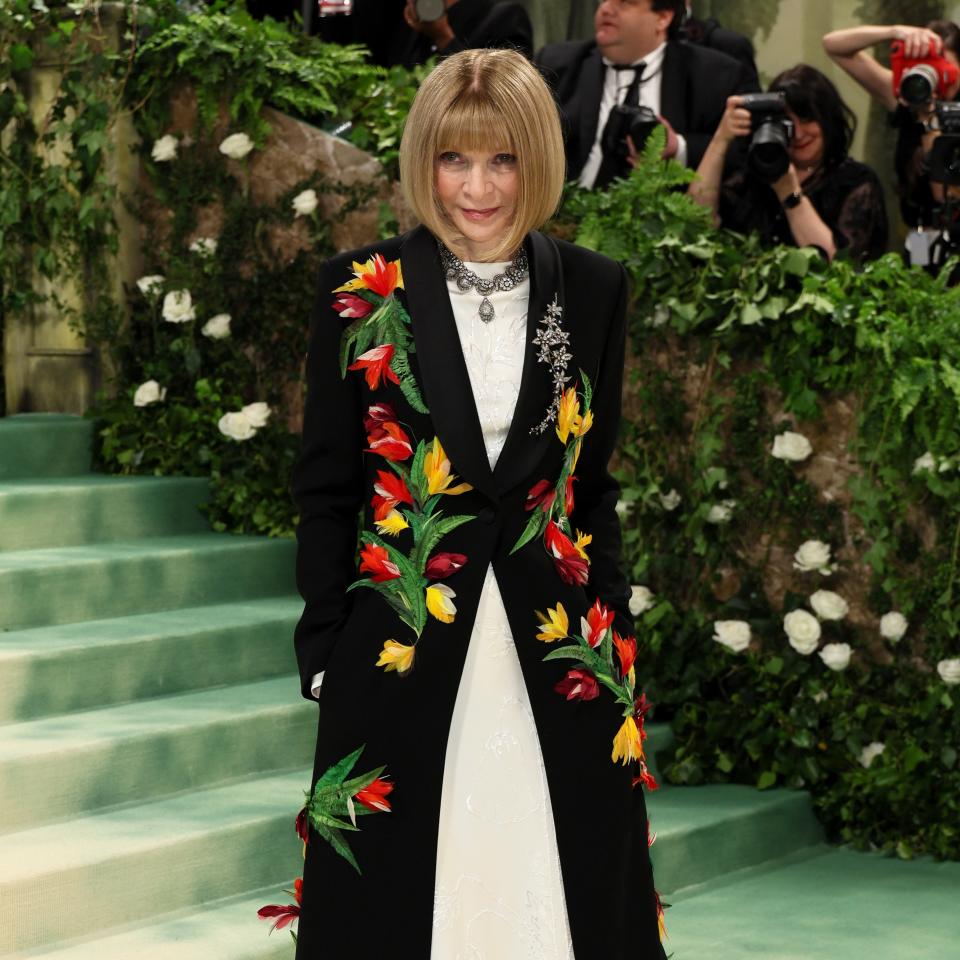 Anna Wintour in a black coat with colorful floral embroidery over a white dress at an event