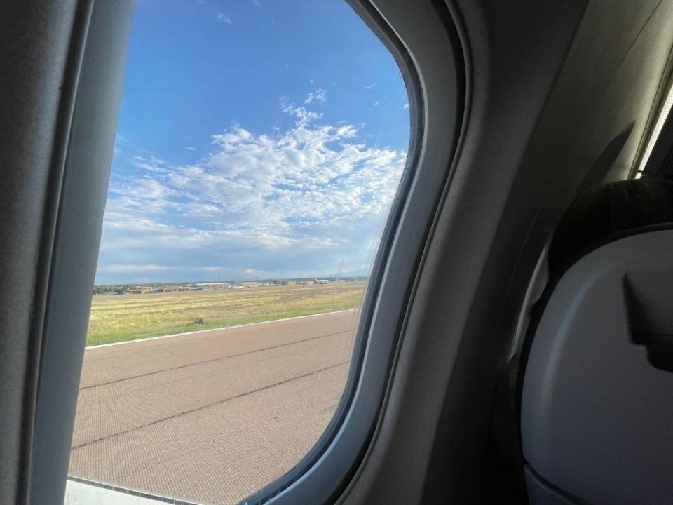 A photo taken from the window of an airplane shows the runway and blue skies.