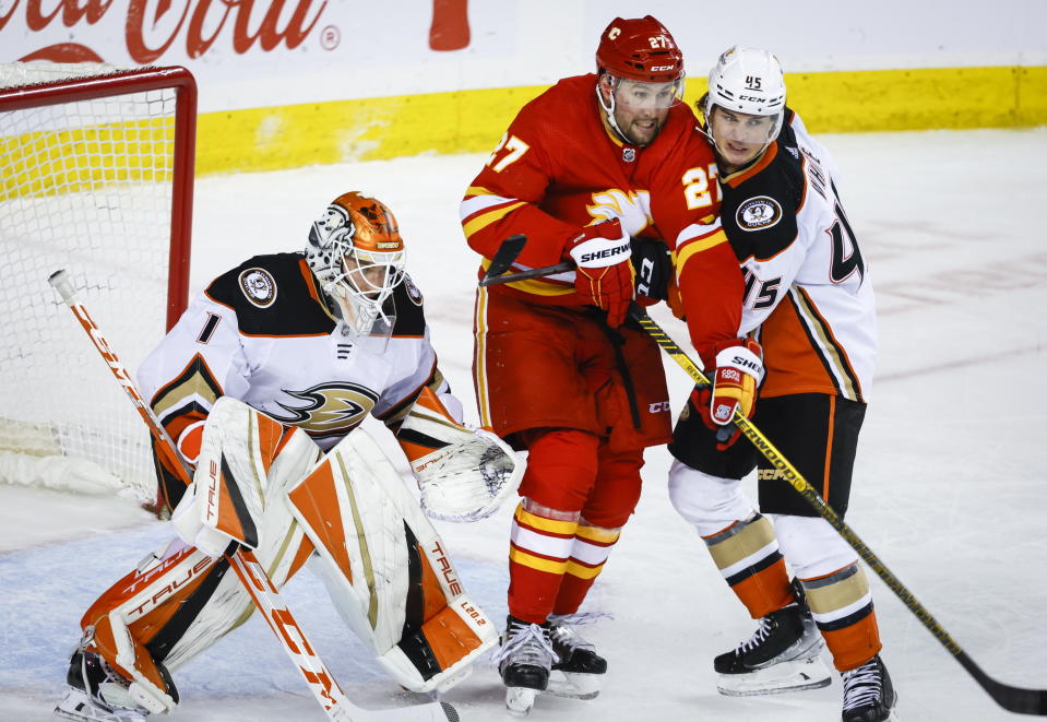 Anaheim Ducks defenseman Colton White, right, checks Calgary Flames forward Nick Ritchie, center, in front of Ducks goalie Lukas Dostal during third-period NHL hockey game action in Calgary, Alberta, Sunday, April 2, 2023. (Jeff McIntosh/The Canadian Press via AP)