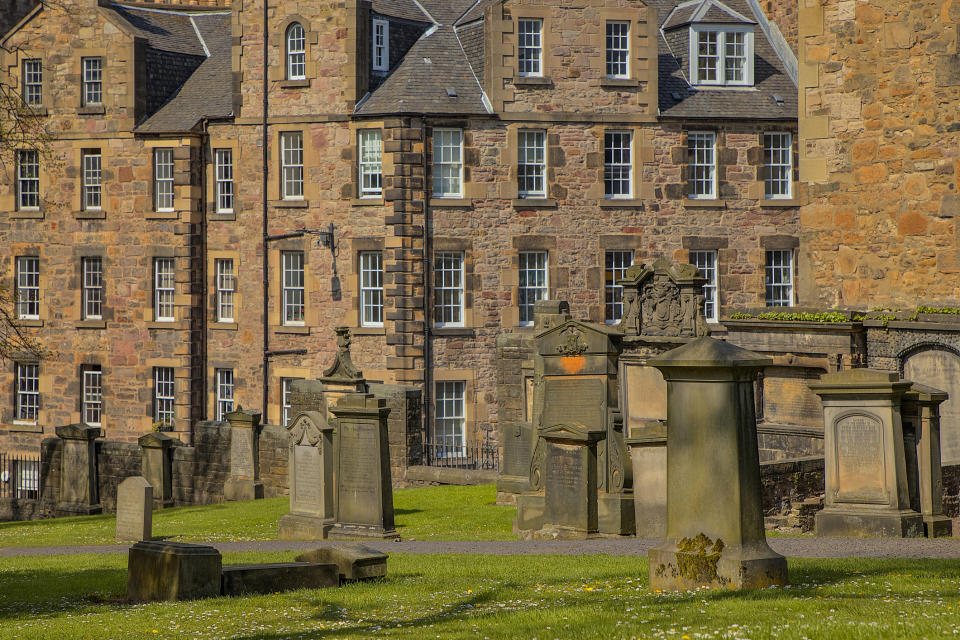 Old cemetery with gravestones in front of a historic building, surrounded by greenery