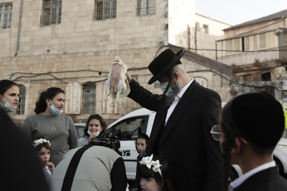 An ultra-Orthodox Jewish man swings a chicken over his family's heads as part of the Kaparot ritual in Jerusalem, Wednesday, Sept. 23, 2020. Observant Jews believe the ritual transfers one's sins from the past year into the chicken, and is performed before the Day of Atonement, Yom Kippur, the holiest day in the Jewish year, which takes place this year during a nationwide three-week lockdown to curb the spread of the coronavirus. (AP Photo/Maya Alleruzzo)