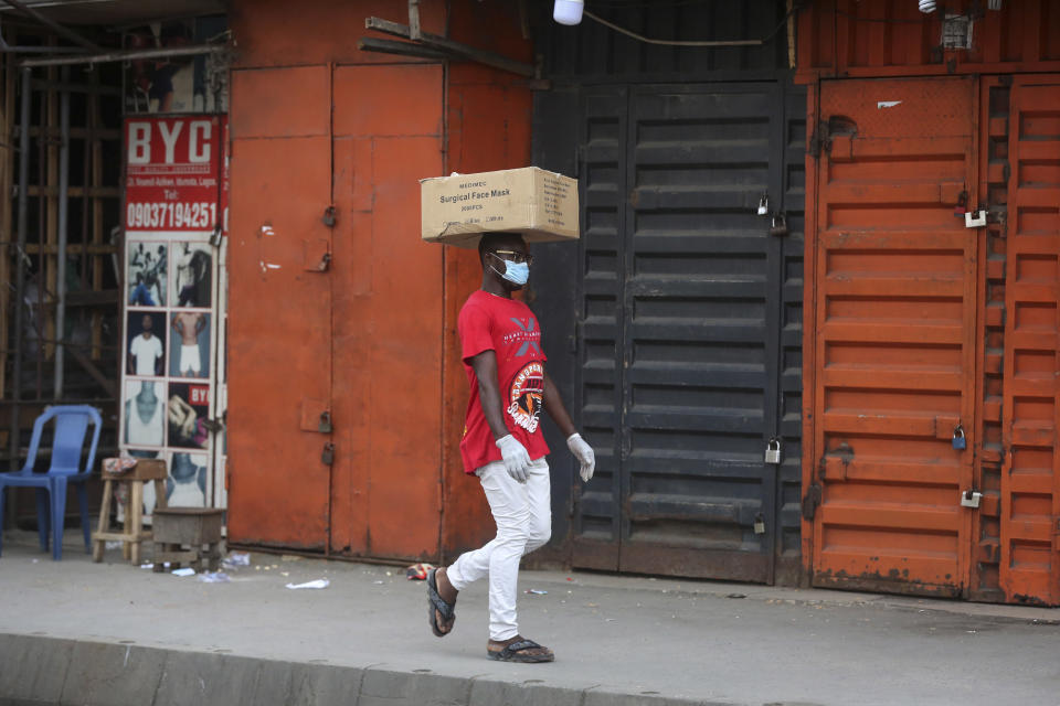 A man carries a box of surgical face masks on his head while wearing one, as he walks past closed shops due to a government ban on the operation of non-essential businesses and markets to halt the spread of the new coronavirus, in Lagos, Nigeria Thursday, March 26, 2020. The new coronavirus causes mild or moderate symptoms for most people, but for some, especially older adults and people with existing health problems, it can cause more severe illness or death. (AP Photo/Sunday Alamba)