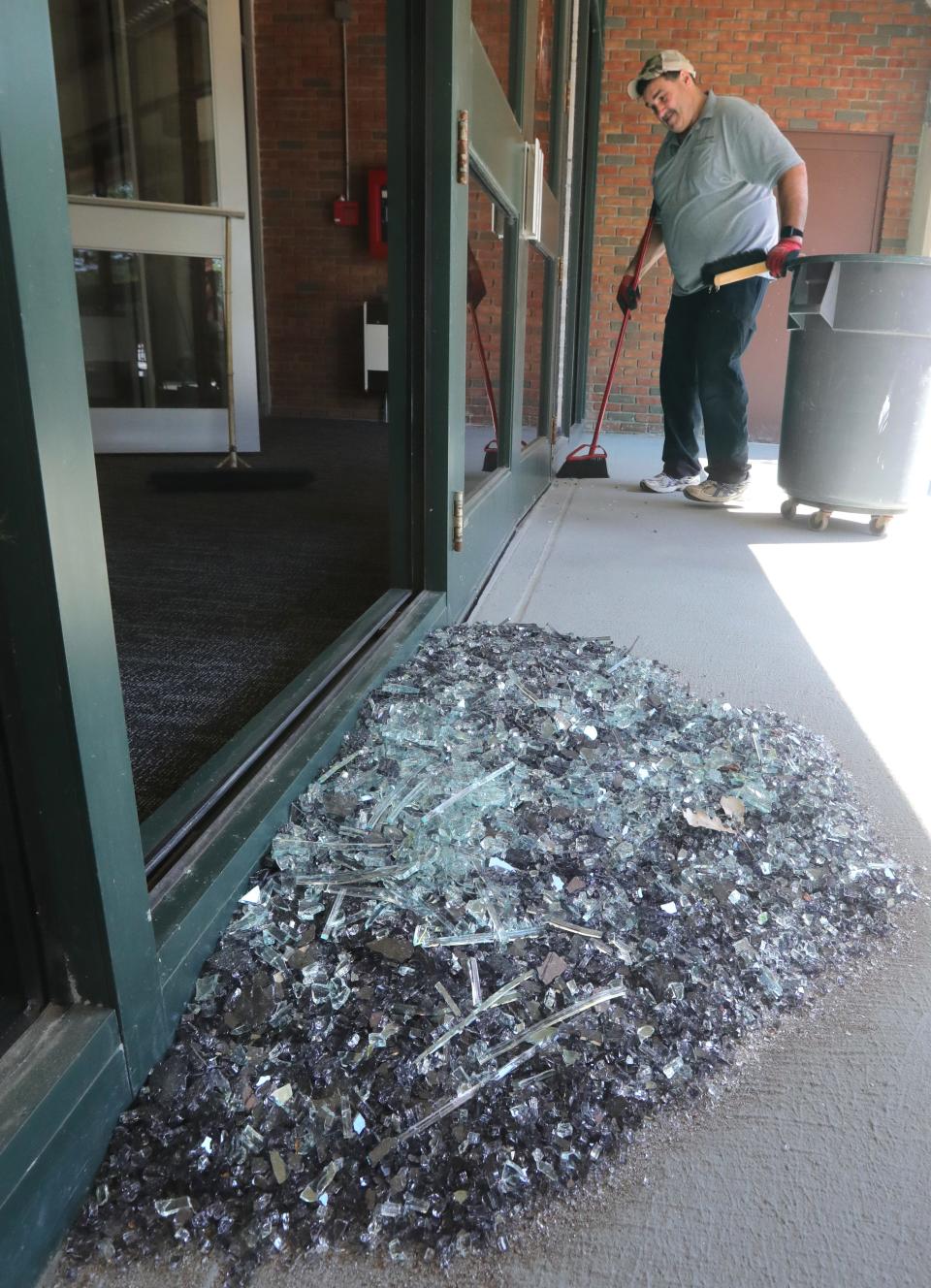 Ken Beery sweeps up broken glass Monday at the entrance of the AES Building on South Main Street in Akron caused by protesters the night before.