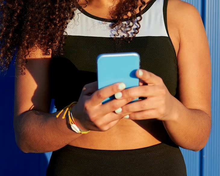 Black female athlete using mobile phone in front of blue wall, looking up doctors for a UTI