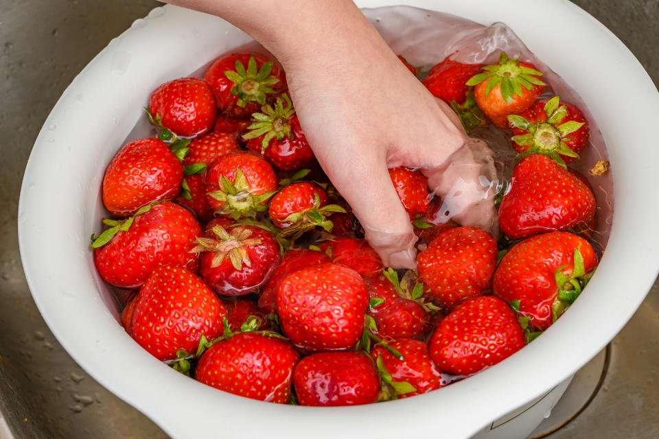 Fresh red strawberries washed after purchase in a bowl of water, mixed by hand, top view, close-up