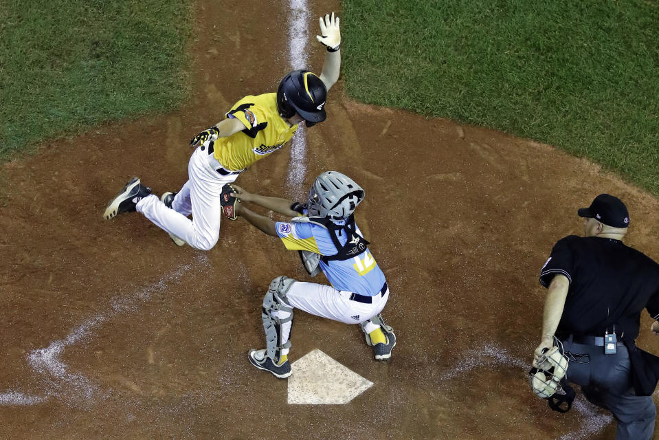 South Riding, Va.'s Chase Obstgarten, left, is tagged out attempting to steal home by Wailuku, Hawaii's Duke Aloy, center, with umpire Matthew Bingaman watching during the third inning of a baseball game at the Little League World Series in South Williamsport, Pa., Wednesday, Aug. 21, 2019. Hawaii won 12-9. (AP Photo/Gene J. Puskar)