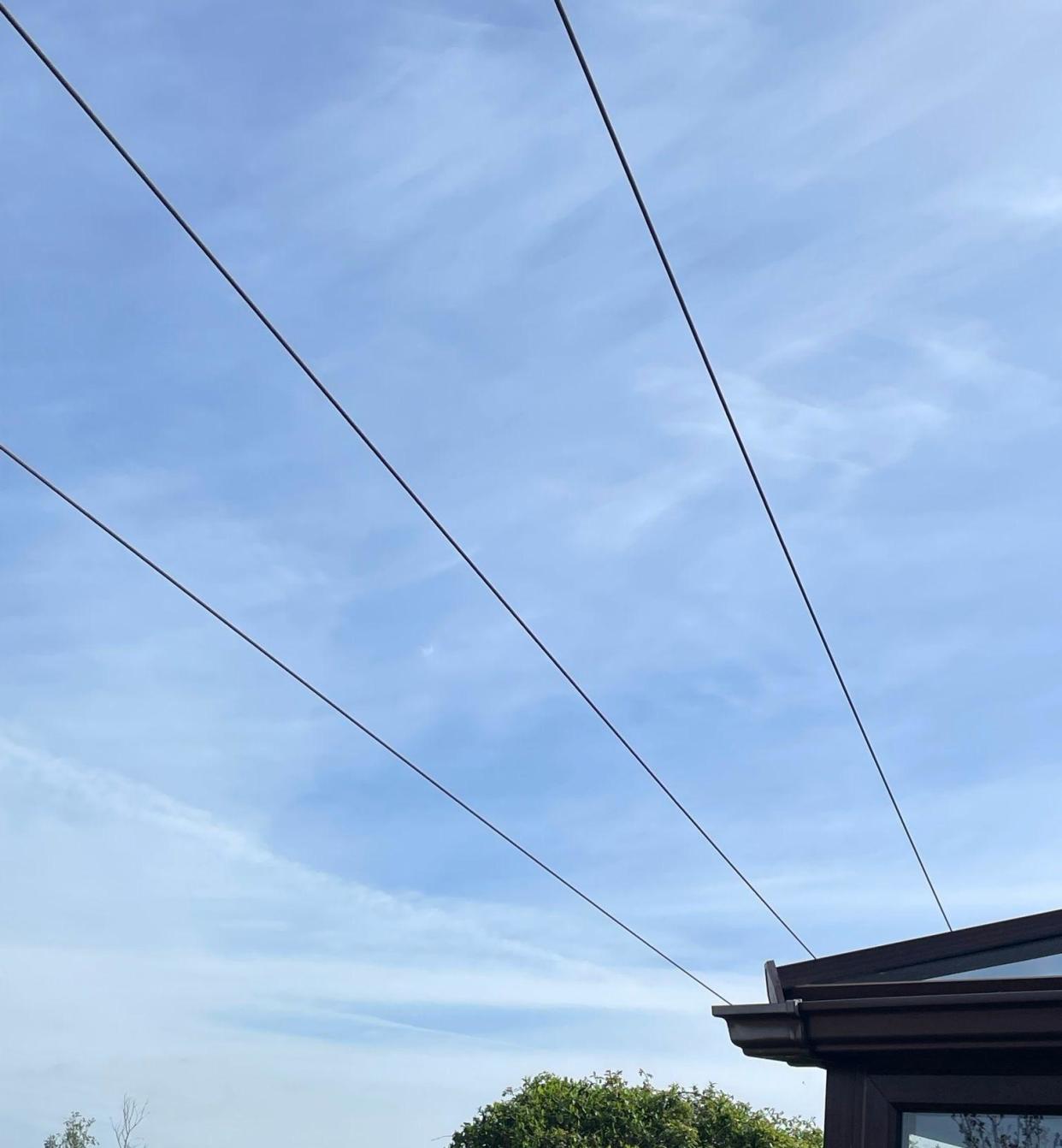A picture of the power lines, which can be seen suspended above the garden against a blue sky. 