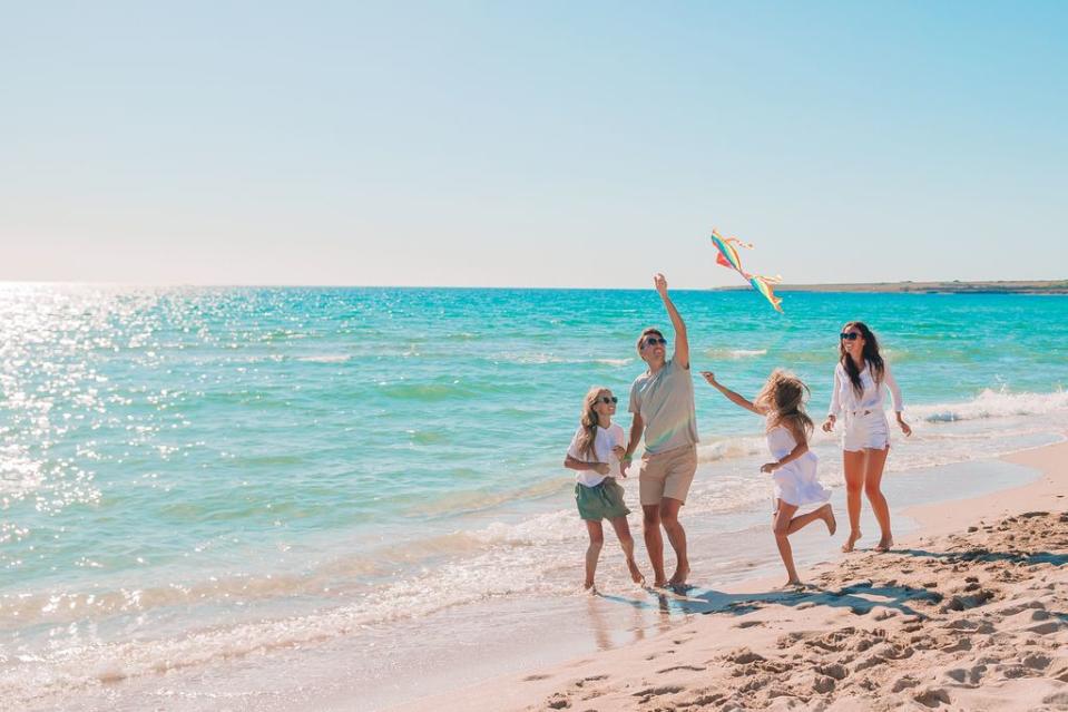 familia feliz de vacaciones en la playa volando una cometa