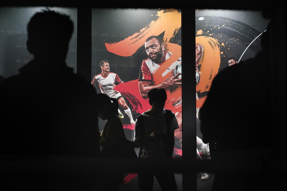 People are silhouetted against an advertisement showing an image of Japan captain Michael Leitch outside an official merchandise store of the Rugby World Cup Wednesday, Sept. 18, 2019, in Tokyo. (AP Photo/Jae C. Hong)