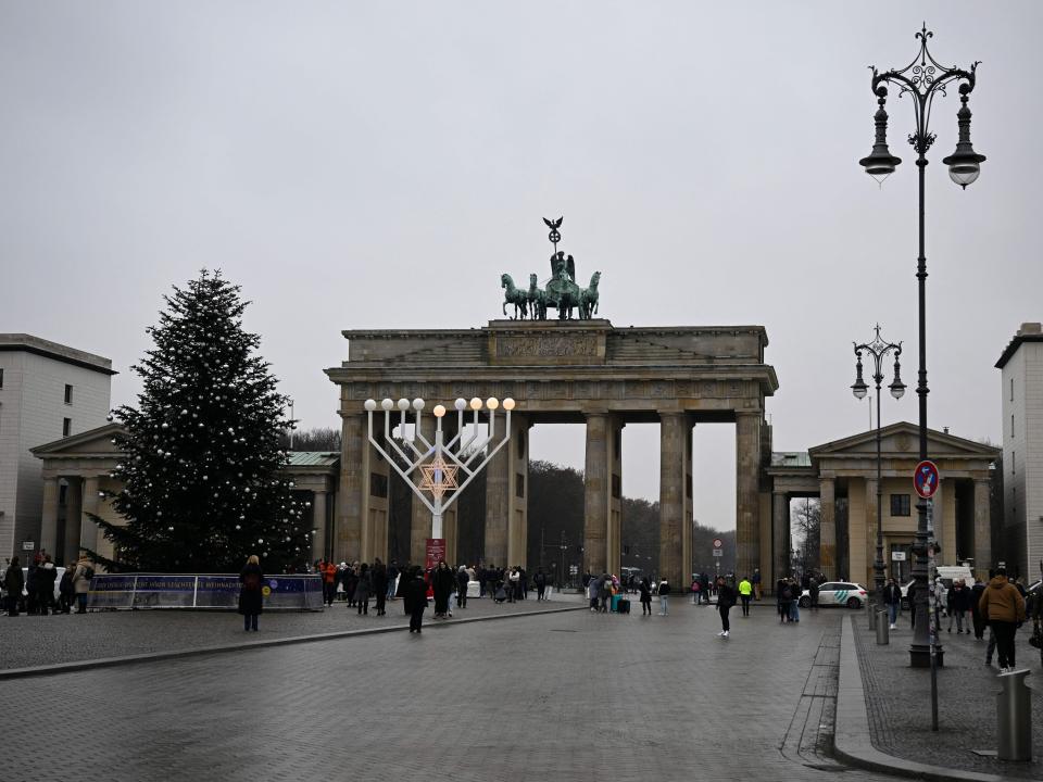 A Christmas tree (L) with its top chopped off is seen next to a Chanukkah menorah in front of Berlin's landmark the Brandenburg Gate on December 21, 2022