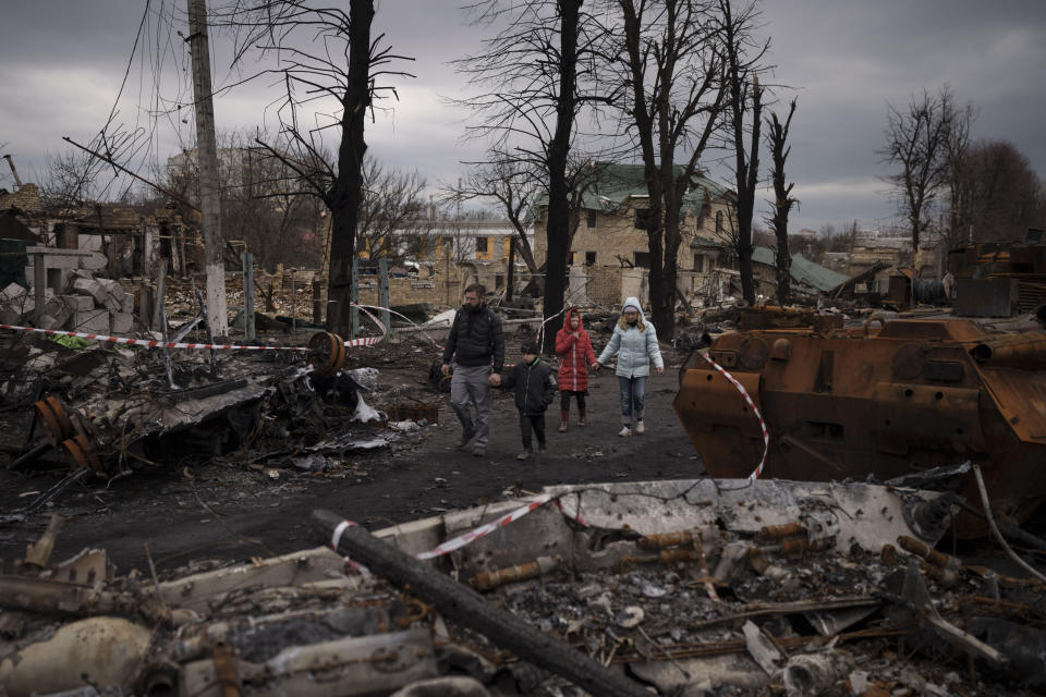 FILE - A family walks amid destroyed Russian tanks in Bucha, on the outskirts of Kyiv, Ukraine, Wednesday, April 6, 2022. The scenes that emerged from this town near Kyiv a year ago after it was retaken from Russian forces have indelibly linked its name to the savagery of war. (AP Photo/Felipe Dana, File)