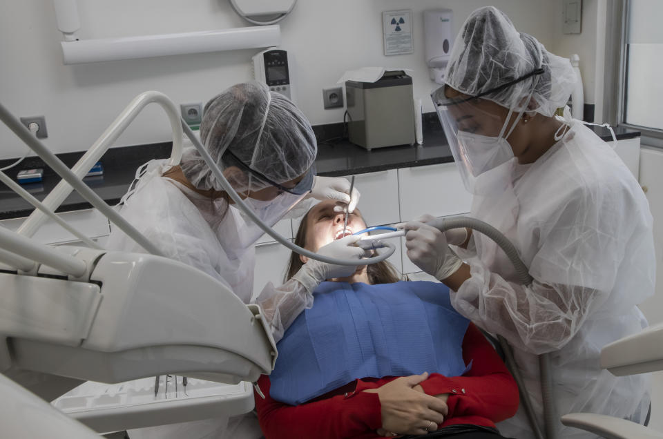 In this Wednesday, May 13, 2020 photo, dentist Sabrine Jendoubi, left, and her dental assistant Margot Daussat inspect the teeth of patient Veronique Guillot, during a dental appointment, at a dental office in Paris. Those with toothache that suffered through France's two-month lockdown, finally have hope to end the pain. Dental practices are cautiously re-opening and non-emergency dentist appointments are now permitted around the country, as the French government eased confinement restrictions from Monday. (AP Photo/Michel Euler)