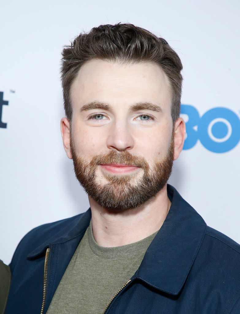 Chris Evans smiling at an event, wearing a dark jacket over a casual shirt