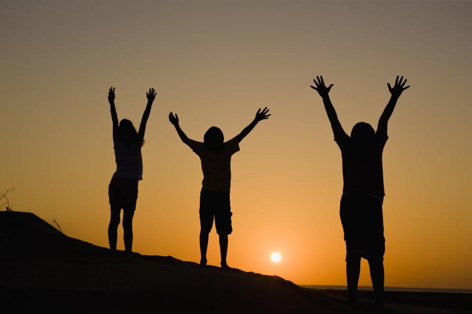 three people enjoying the sunset while raising arms