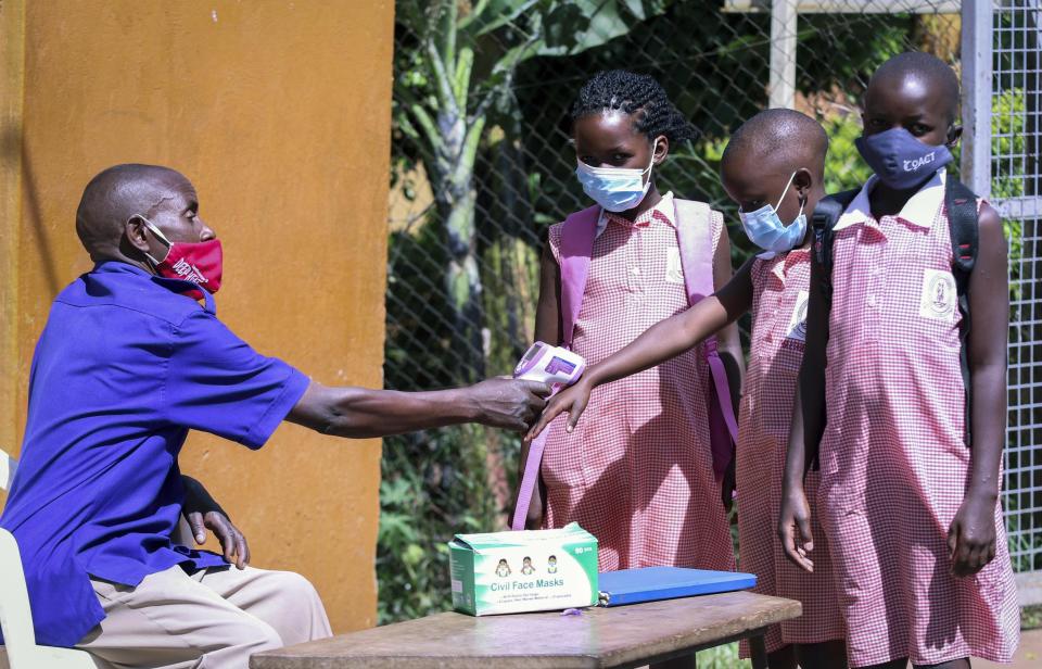 A school security guard measures the temperature of the pupils at the entrance of Kitante Primary School in Kampala, Uganda Monday, Jan. 10, 2022. Uganda's schools reopened to students on Monday, ending the world's longest school disruption due to the COVID-19 pandemic. (AP Photo/Hajarah Nalwadda)