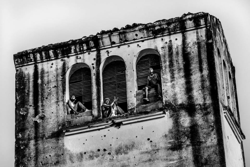 Men are seen seated in what used to be a bell tower high up on a building.