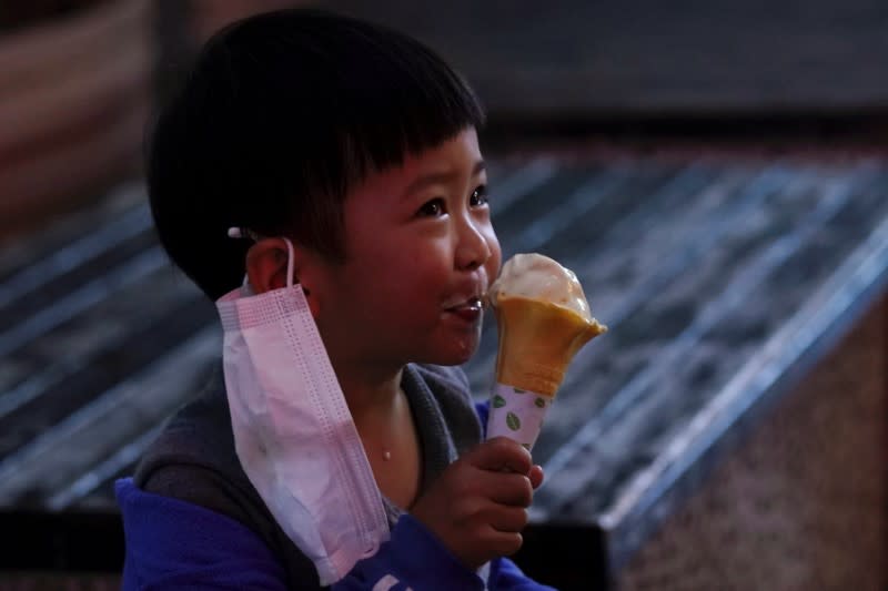 Child with a face mask eats an ice cream outside the ice cream store on its first day of opening following the coronavirus disease (COVID-19) outbreak, in Xianning