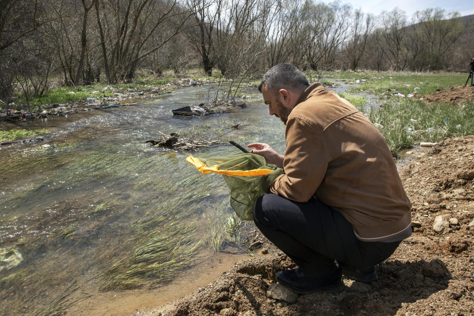 Halil Ibrahimi, 44, associate professor at the faculty of natural sciences at Pristina university searches his net for insects near a polluted stream in Siceve, Kosovo, Friday, April 16, 2021. Restrictions during the coronavirus pandemic helped Kosovar biologist Ibrahimi sit down and complete his research, naming a new insect after the virus and raised public awareness against pollution of river basins. (AP Photo/Visar Kryeziu)