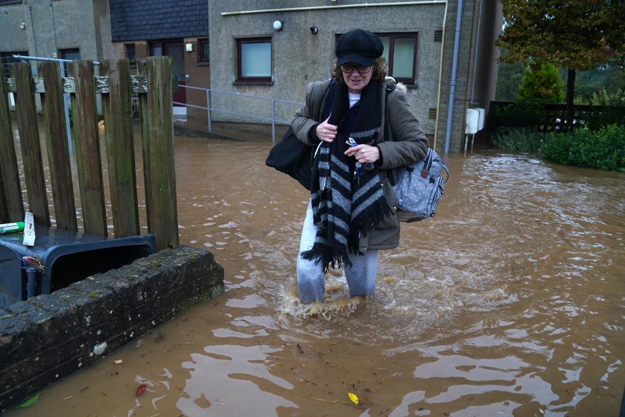 A woman wades through floodwater while clutching her belongings after Storm Babet battered Brechin, Scotland (PA)